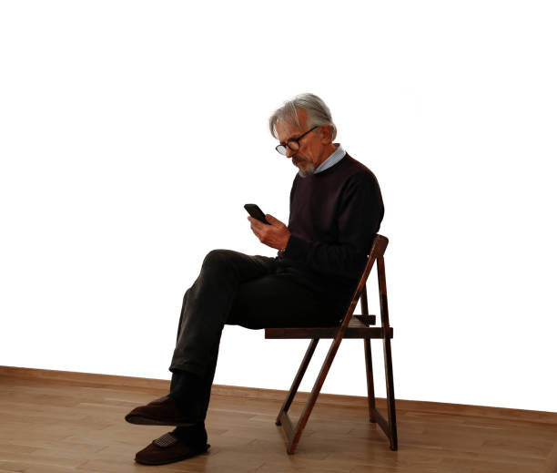 Elder man sits on the chair and uses a  mobile phone. White background. Moving into a new apartment. Empty flat
