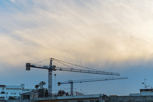 Two tower-type construction cranes on the background of a wide cyclonic cloud, changing weather conditions during various works.