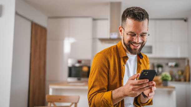 man with eyeglasses stand at home use mobile phone sms texting