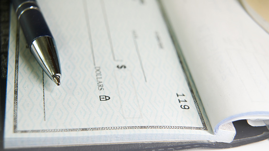 A black pen is poised on a blank check with its tip resting near the payment amount line, ready for someone to fill out the necessary details for a financial transaction.