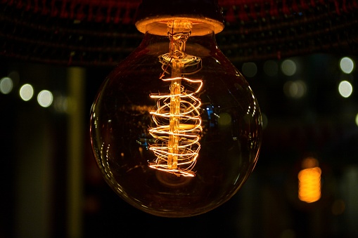 A close up of an incandescent light bulb lit in the dark.