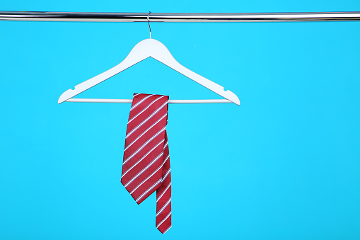 Necktie hanging on wooden hanger on blue background