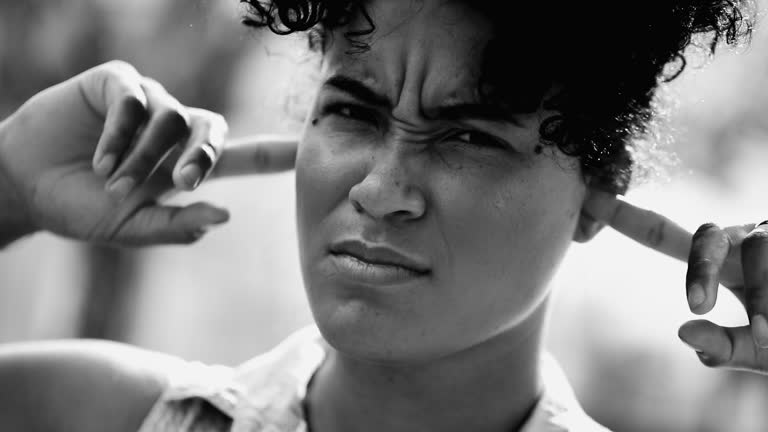 Young Lady Refusing to Listen, Placing Fingers in Ears, Muting External Noise, Dismissive Gesture to Ignore Warnings in black and white