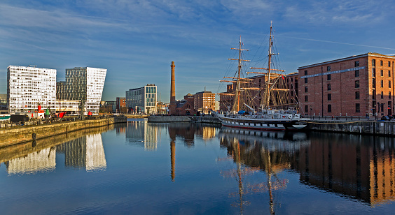 View across the Albert Dock in the centre of Liverpool, UK.  A tall ship can be seen moored in the dock and people can be seen on the promenade.