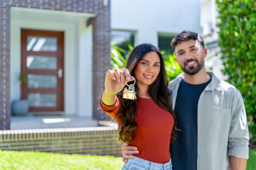 happy woman and man, holding keys from new first house, young family celebrating moving day, satisfied customers couple purchase real estate, mortgage and relocation concept. The building can be seen in the background