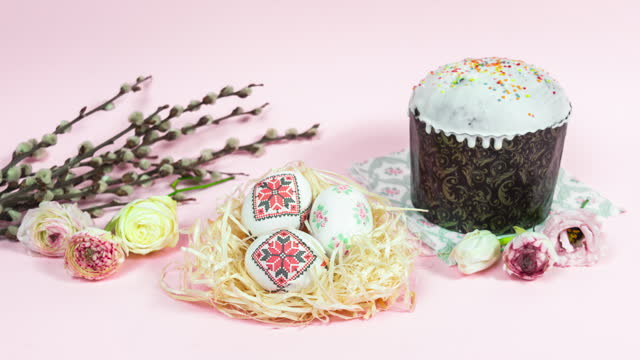 Painted Easter eggs move cyclically. Easter cupcake and willow branches are decorated with natural fresh flower heads. Light pink background.