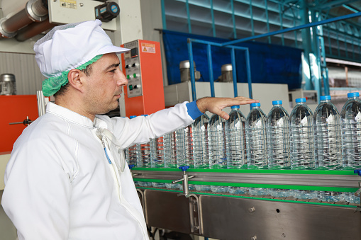 On the production line of a water industry factory, an industrial quality inspector audits and purifies water by inspecting water bottles on an automated conveyor belt.