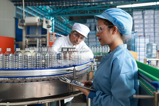 The lab technicians and hygienists with clean suits and PPE examining water bottles in bottling plant mineral water drinking water factory