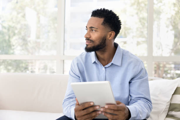 Positive thoughtful young African American man using digital tablet