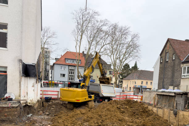 A small construction site where an yellow excavator loads soil onto a truck.