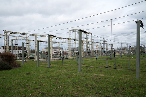 Substation with many electrical wires and metal masts. Gray cloudy sky.