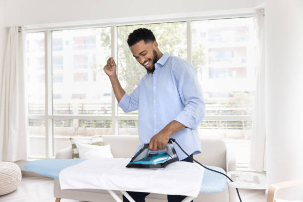istock Cheerful Black man enjoying house work, ironing white fabric towel 2066576311