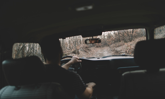 Cabin view of man driving off-road vehicle through the forest, selective focus.