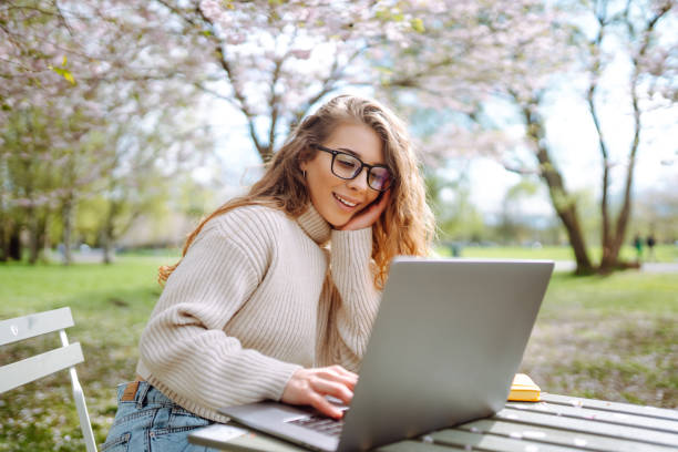 istock Beautiful woman sitting on blooming park and using laptop. 2066618816