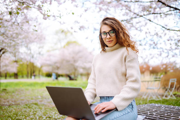 istock Beautiful woman sitting on blooming park and using laptop. 2066618820