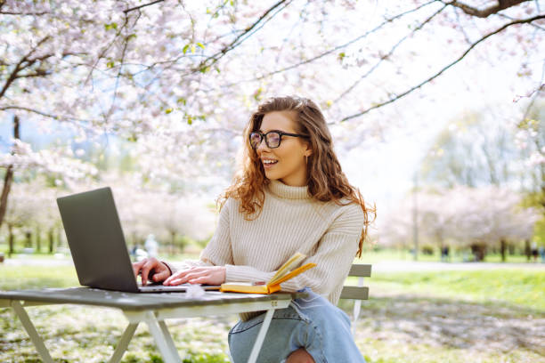 istock Beautiful woman sitting on blooming park and using laptop. 2066619353