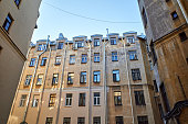 View from below of old courtyard yellow wall in St. Petersburg, Russia. Wall, windows, tubes and part of blue sky