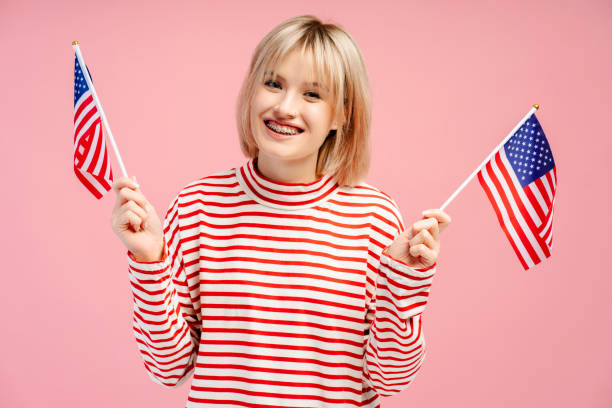 Smiling young woman with braces holding American flags, looking at camera, posing isolated