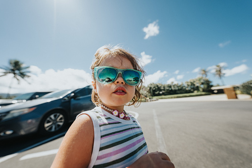 Cute Eurasian toddler girl waiting by her family's car in sunny parking lot