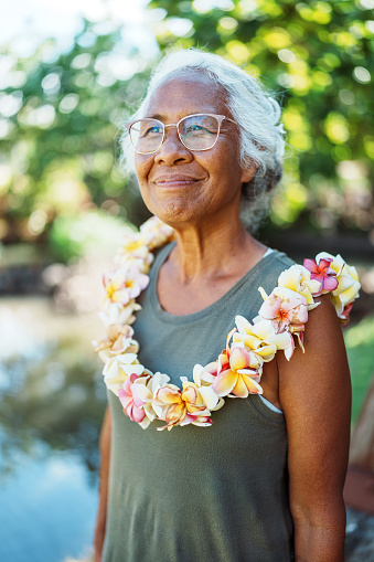 Portrait of an active and healthy senior woman of Hawaiian and Chinese descent wearing a plumeria lei smiling with confidence and gratitude while spending time outdoors.