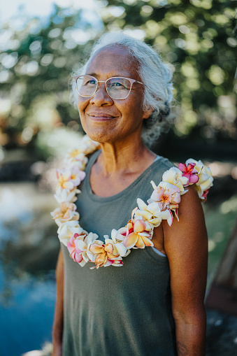 Portrait of an active and healthy senior woman of Hawaiian and Chinese descent wearing a plumeria lei smiling with confidence and gratitude while spending time outdoors.