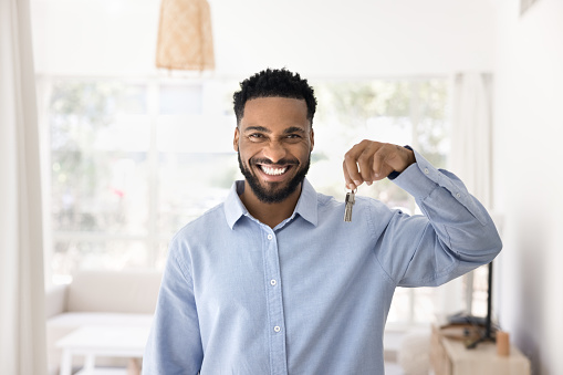 Cheerful young African new homeowner man holding key from new apartment, looking at camera, smiling, celebrating house buying, real estate property ownership, posing for portrait