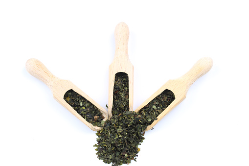 Green tea with herbs in wooden spoons on a white background