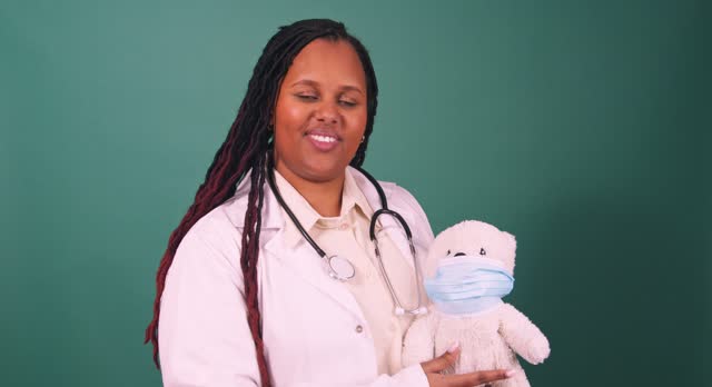 Video of young Black female doctor demonstrating face mask with teddy bear