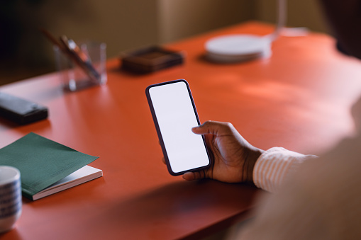 Close-up of a hand holding a smartphone with a white screen, set on a desk with office supplies.