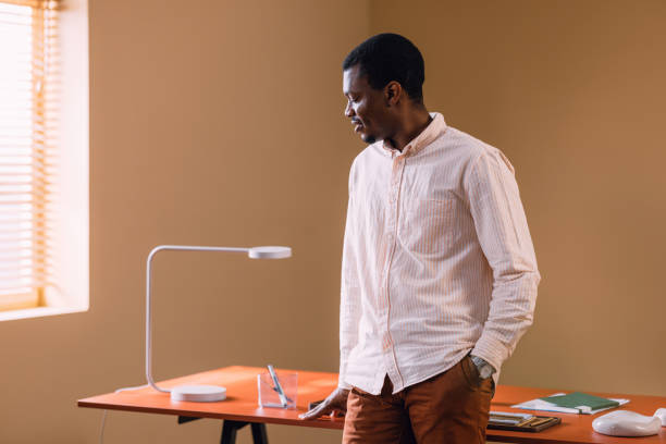 istock Thoughtful Man Standing Alone at Minimalist Workspace with Desk Lamp 2066722221