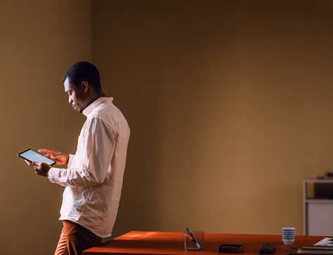 Focused African man working on a digital tablet while standing in a modern office setting with minimalist decor.