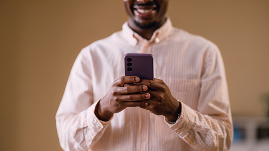 Cheerful African American man capturing a selfie with his purple smartphone, expressing happiness and technology usage.