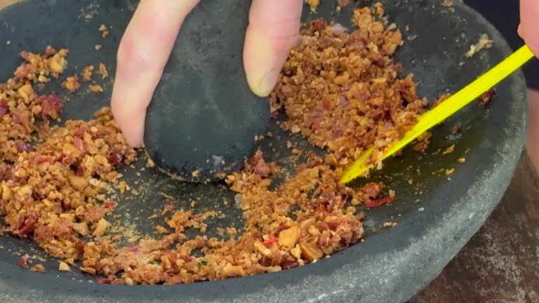 A home cook uses a mortar and pestle to grind peanuts and chilli into a satay sauce for use in traditional Indonesian cooking