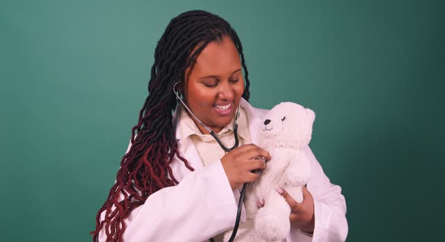 Young Black female doctor demonstrating monitoring heartbeat with a teddy bear