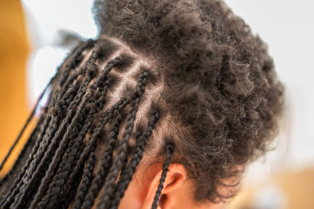 Close-up view of a mixed race female and a mid adult Black female engaging in braiding hair at home.