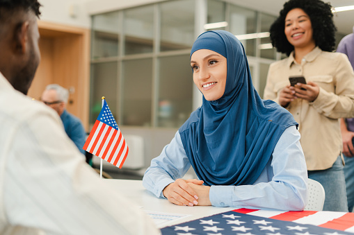 Smiling woman wearing hijab waiting in line voters registration at polling station. Democracy, vote, US presidential election concept