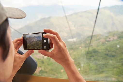 Unrecognizable young person taking photos with his phone from inside a cable car cabin in the Chicamocha Canyon, in Santander, Colombia.