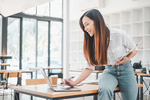 A vibrant entrepreneur adjusts her laptop in a bright workspace, her posture exuding confidence and adaptability, hallmark traits of successful business agility.