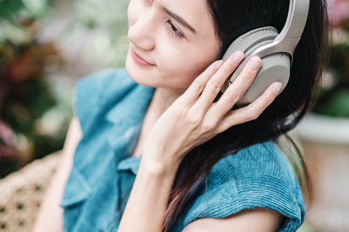A close up of a serene woman adjusting her headphones, immersed in the soundscape of her tranquil garden environment.