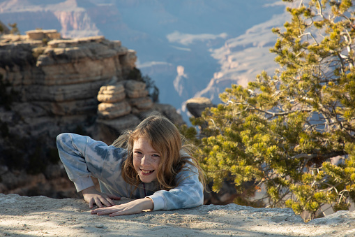 Girl is smiling at the camera as she pretends to pull herself up the cliff at the Grand Canyon