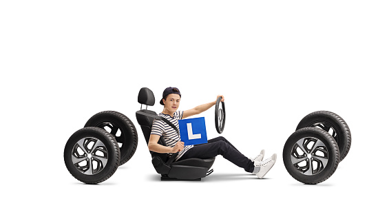 Teenage male driver in a car seat holding L-plate isolated on white background