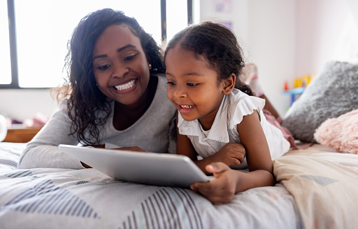 African American girl reading a book online under the supervision of her mother and smiling