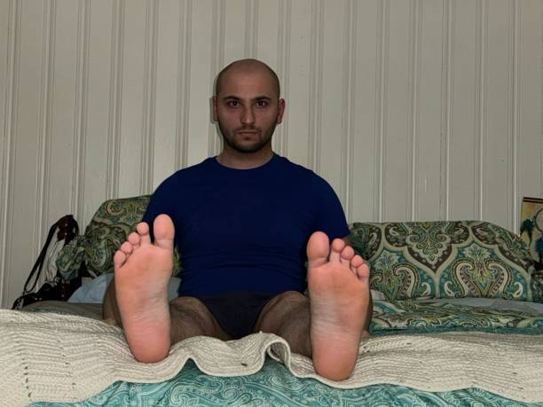 23 year old male sitting on bed, blue shirt, bare feet