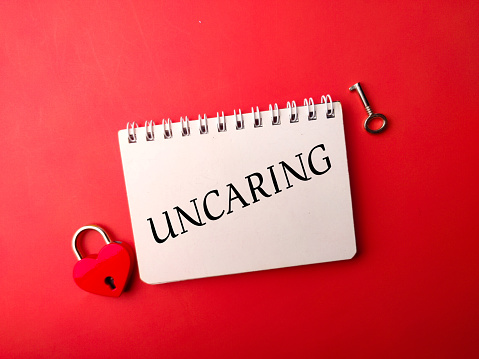 Notebook and love padlock with the word UNCARING on a red background