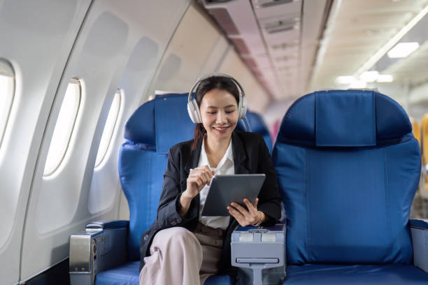 uma mulher está sentada em um assento de avião azul com um tablet na mão - room service audio - fotografias e filmes do acervo