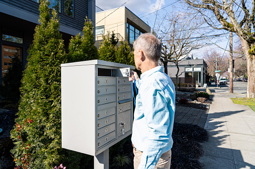 Mailman's arm inserting a bundle of mail into a mailbox.  Partially obscured suburban home in background.  Horizontal orientation.