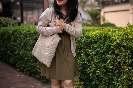 A cropped shot of a happy Asian woman in casual clothes walking in the city on a bright day. people and lifestyle concepts