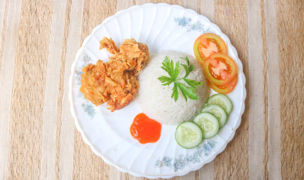 istock Crispy fried chicken with spicy sauce is served with rice and vegetables such as cucumber, tomato and celery as garnish. Fried chicken and rice on wooden table 2067372402