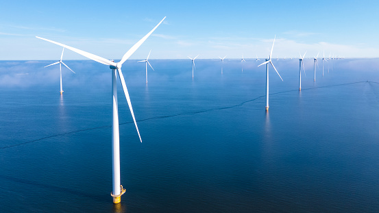 Windmill park in the ocean, drone aerial view of windmill turbines generating green energy electrically, windmills isolated at sea in the Netherlands with a blue sky at summer