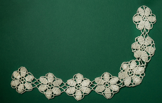 Handmade crochet lace in bege on a  green background.